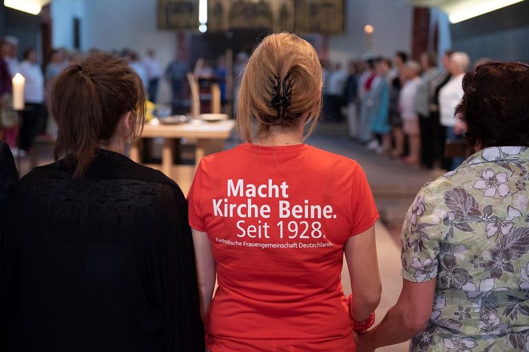 Demonstrationsteilnehmerin mit Aufdruck „Macht Kirche Beine. Seit 1928“ auf dem T-Shirt.