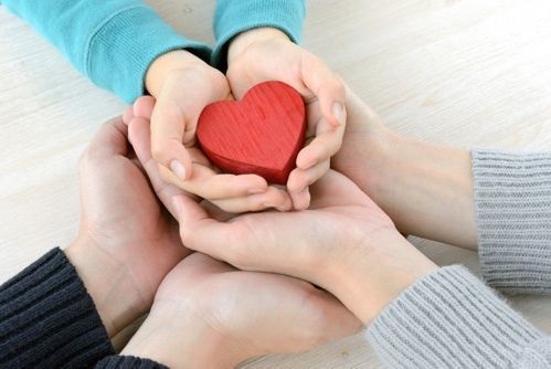 Zusammenhalten: Hände umfassen ein rotes Herz als Symbol der Verbundenheit und Liebe.