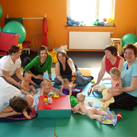 Gruppe von Eltern und Kindern bei einer Babyturnstunde mit Übungen auf Matten.
